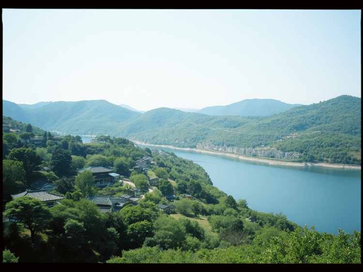 A panoramic view of a serene river winding through lush green hills, with traditional houses scattered along the shoreline under a clear blue sky.